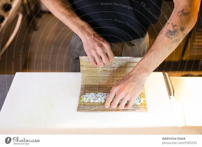 Anonymer Mann, der mit einer Bambusmatte eine Rolle macht Küchenchef anonym rollen Sushi Unterlage Tisch Werkzeug vorbereiten Arbeitsplatz männlich Job