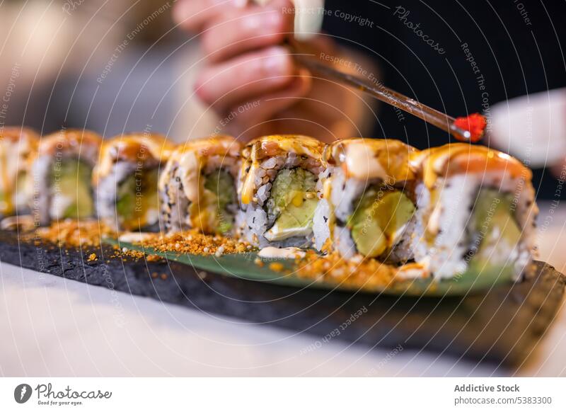 Unbekannte Person serviert Tobiko auf Uramaki-Sushi-Rollen mit Stäbchen Essstäbchen tobiko rollen Reis dienen Meeresfrüchte Tablett lecker Avocado
