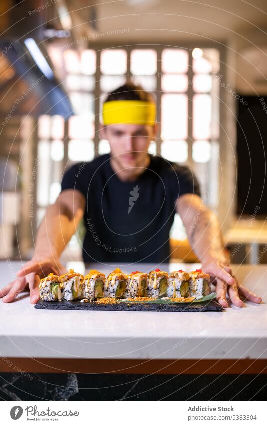 Junger Mann präsentiert Tablett mit Uramaki-Sushi-Rollen auf dem Tisch rollen Avocado Reis dienen lecker Lebensmittel Küche jung männlich Asiatische Küche