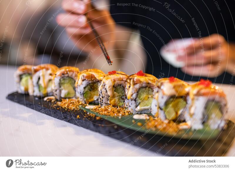 Unbekannte Person serviert Tobiko auf Uramaki-Sushi-Rollen mit Stäbchen Essstäbchen anonym tobiko rollen Reis dienen Meeresfrüchte Tablett lecker Avocado