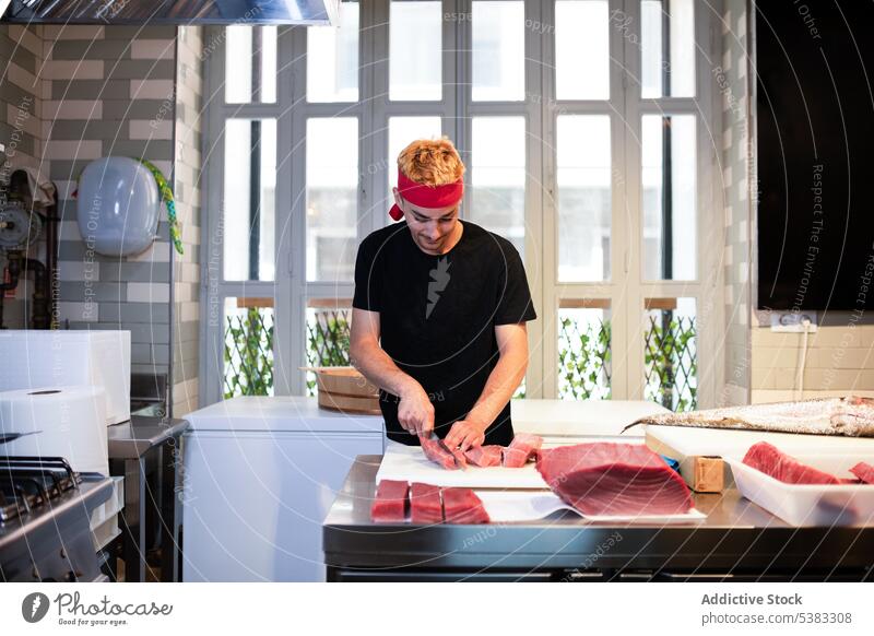 Konzentrierter junger Mann, der Thunfischfleisch schneidet geschnitten rot frisch roh Tisch Konzentration Fokus Küche männlich Koch Lebensmittel Fisch
