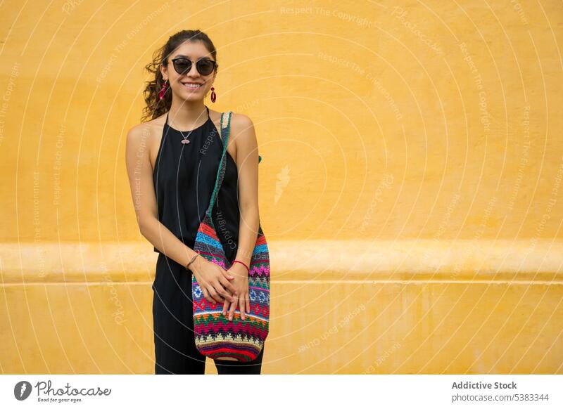 Glückliche junge Frau mit Tasche Lächeln Stil Outfit Wand gestrickt Ornament Sonnenbrille Mexiko San Cristobal de las Casas Chiapas farbenfroh Mode trendy