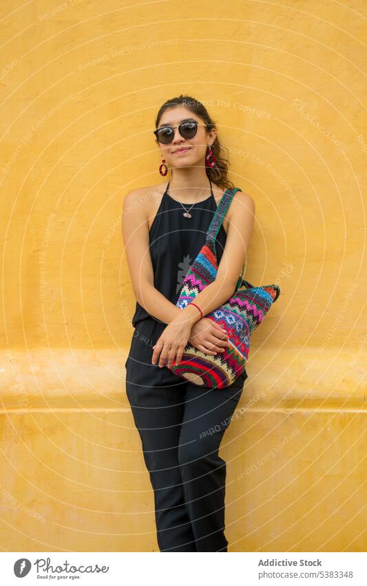 Positive junge Frau mit Tasche Stil Outfit Wand gestrickt Ornament Sonnenbrille Mexiko San Cristobal de las Casas Chiapas farbenfroh Mode trendy hell positiv