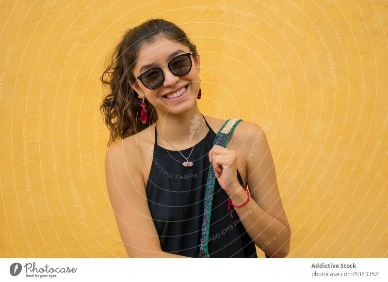 Glückliche junge Frau mit Tasche Lächeln Stil Outfit Wand gestrickt Ornament Sonnenbrille Mexiko San Cristobal de las Casas Chiapas farbenfroh Mode trendy