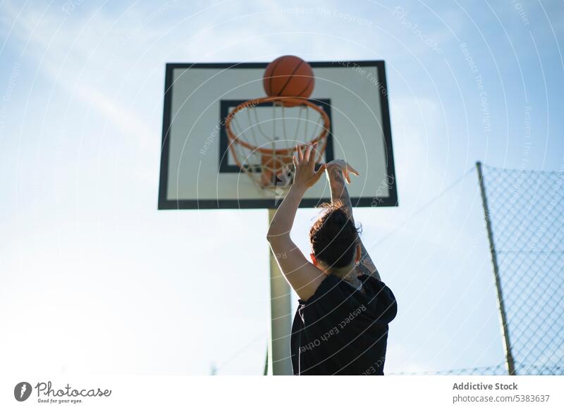 Sportlerin spielt Basketball auf einem Platz im Sonnenlicht unkenntlich Spieler Sportpark werfen Reifen Plakatwand Streetball Gericht Frau maskulin schießen