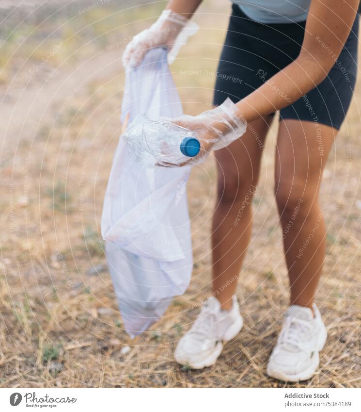 Anonyme Erntehelferin, die Müll vom Boden aufhebt Aktivist Tasche Flasche Pflege Sauberkeit abholen sammelnd Tag dreckig Erde Ökologie Umwelt Wald Handschuh