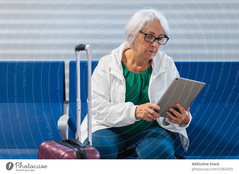 Ernste ältere Frau mit Tablette Rentnerin in den Ruhestand gehen benutzend zuschauen Warteraum reisen Film warten ruhen Gepäck Browsen Video Gerät Apparatur