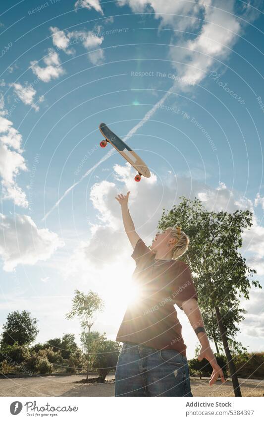 Aufgeregter Junge wirft Skateboard in den Himmel Frau Wildfang aufgeregt werfen androgyn Arm angehoben erreichen Spaß Freude wolkig Blauer Himmel Landschaft
