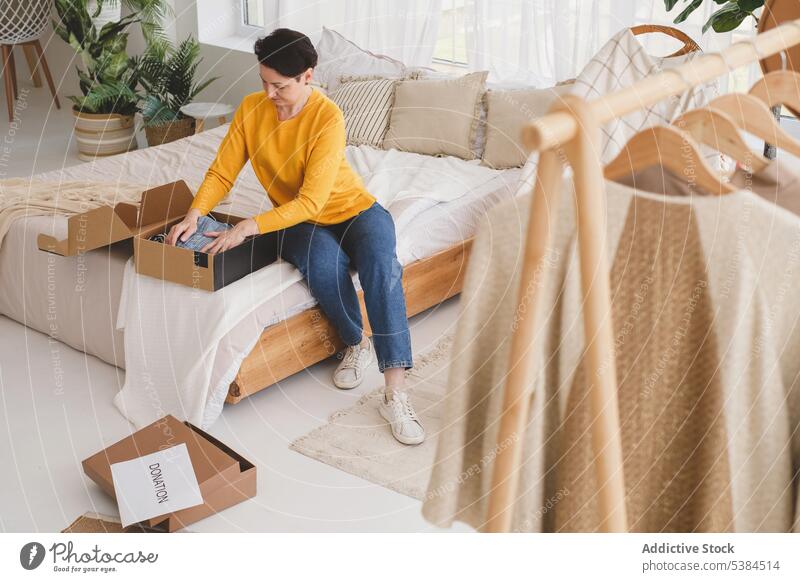 Konzentrierte Frau verpackt Kleidung für eine Spende Fokus Konzentration schenken Geldgeschenk Almosen Rudel Paket Kasten zu Hause Windstille Schlafzimmer Bett