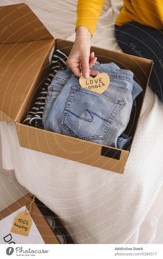 Crop Frau packt Kleidung in Karton Stoff Rudel Geldgeschenk Almosen schenken Hinweis Geschenk Paket Kasten Jeanshose Schachtel Papier Herz Tasche lässig