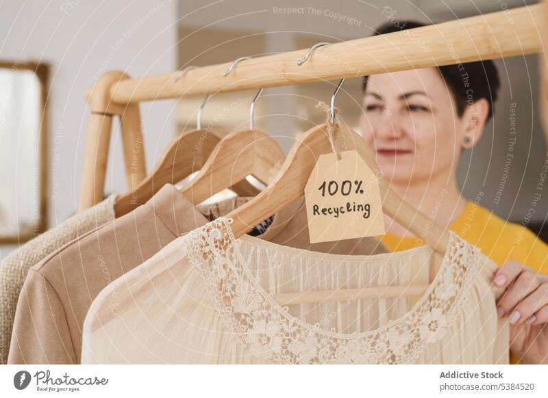Unscharfe Frau in der Nähe der auf Holzbügeln hängenden Kleidung Stoff Kleiderbügel Ablage Aufschrift wiederverwerten Kleidungsstück Tag kennzeichnen