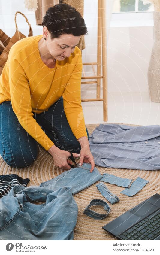 Frau schneidet Kleidung Konzentration Fokus Rudel Stoff Laptop Paket vorbereiten zu Hause Bekleidung heimwärts Wohnzimmer benutzend Apparatur Arbeit Kurze Haare