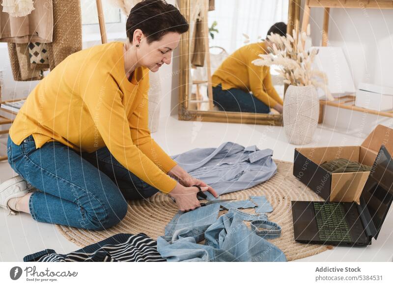 Frau schneidet Kleidung in der Nähe des Laptops Konzentration Fokus Rudel Stoff Paket vorbereiten zu Hause Bekleidung heimwärts Wohnzimmer benutzend Apparatur