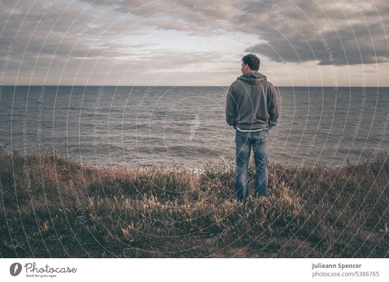 Mann auf Klippe mit Blick aufs Meer allein MEER Feld Wasser loneyl Küste Landschaft Jeanshose Kapuzenpulli desolat deprimiert AUFGEBEN Meereslandschaft Ufer