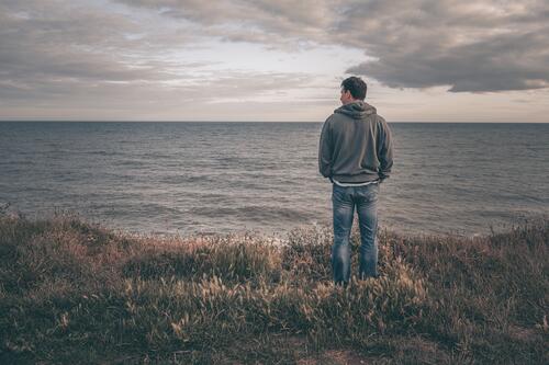Mann auf Klippe mit Blick aufs Meer allein MEER Feld Wasser loneyl Küste Landschaft Jeanshose Kapuzenpulli desolat deprimiert AUFGEBEN Meereslandschaft Ufer