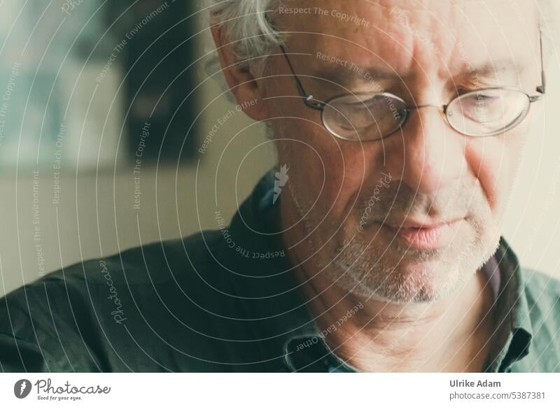 Mainfux | Mann mit Brille schaut nachdenklich und versunken nach unten Blick nach unten Hintergrund neutral Stirn ernst Konzentration geduldig lesen Denken