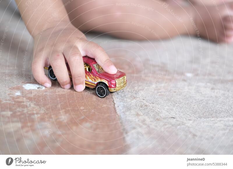 Kinderhand mit Spielauto am Boden Kindergarten Kindheit Tagesstätten Kinderspiel Kita kreativ naiv kindlich Spielen lernen erziehen Erziehung Grundschule