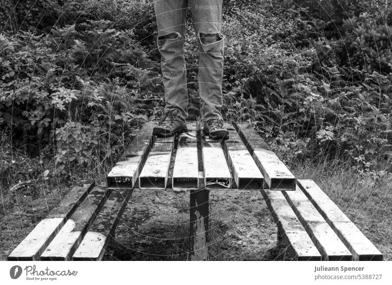 Mann steht auf verlassenem Metall-Picknicktisch Picknick-Tisch Picknickbank Verlassen Menschenleer schwarz auf weiß Wanderschuhe zerrissene Jeans rustikal alt