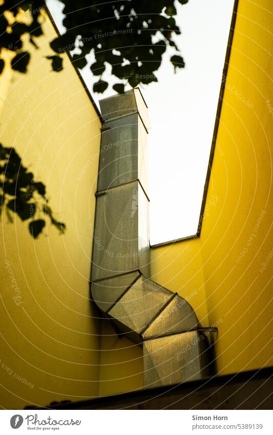 Kamin in einem verwinkelten Hinterhof Abwärme nach oben gelb Wände eingebaut Flächen flächig schattig Stadt Gebäude Schlot Dunstabzug Bauwerk fensterlos