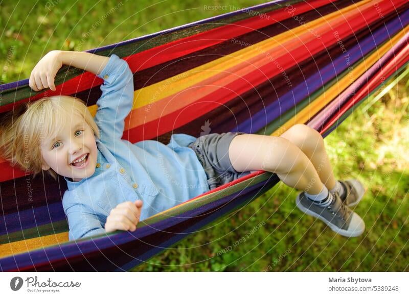 Nette kleine blonde kaukasischen Jungen entspannen und Spaß haben in bunten Hängematte im Hinterhof oder Spielplatz im Freien. Sommer aktive Freizeit für Kinder. Kind schwingt auf Hängematte.
