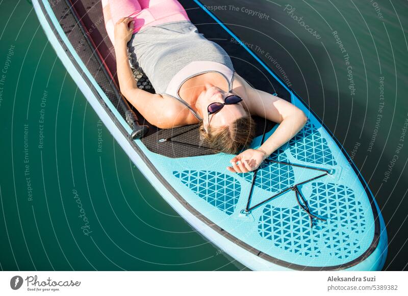 Junge sportliche Frau paddelt auf dem Fluss, auf dem Brett liegend, entspannt unter der Sommersonne aktiv Aktivität Abenteuer attraktiv Strand schön Holzplatte