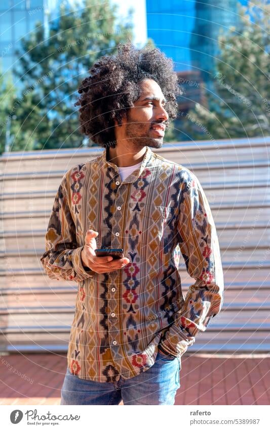 Porträt eines gut aussehenden afroamerikanischen Mannes, der sein Handy auf der Straße benutzt. schwarz Freizeitkleidung Selbstvertrauen Tag Fotografie Telefon