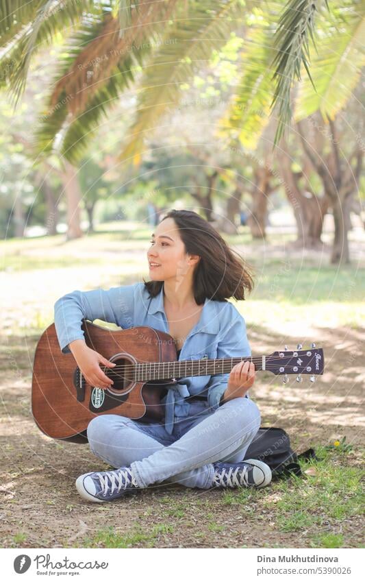 Junge Frau spielt Gitarre im Park im Sommer, sitzen unter der grünen Palme. Millennial Musikerin. Freizeit schön Musical Leistung Entertainment heiter
