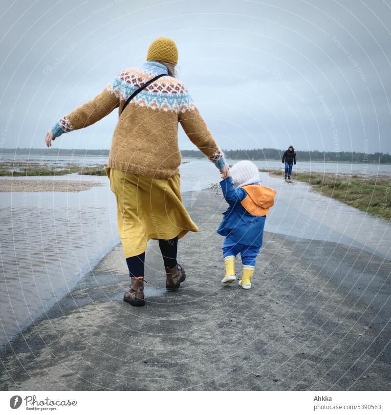 Junge Frau mit kleinem Kind in gelb und blau an einer überfluteten Straße an der Küste Kleinkind Sturm Wasser überflutete Straße extrem laufen Hochwasser