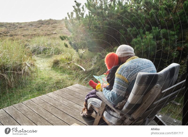 Ein Mann und ein Kind lesen gemeinsam ein Buch auf einer hölzernen Veranda in der Natur Vater Zusammensein Papa zeit verbringen Kindheit erzählen Glück