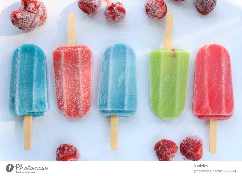 Eiskaltes buntes Eis am Stiel auf einem weißen Hintergrund.  Fruchteis mit gefrorenen Erdbeeren auf einem weißen Hintergrund. Lebensmittel Sommer Sahne