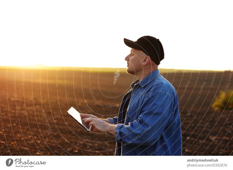 Intelligente Landtechnik und Landwirtschaft. Ein Landwirt benutzt ein digitales Tablet auf einem Feld mit gepflügtem Boden bei Sonnenuntergang. Überprüfung und Kontrolle der Bodenqualität, der Bereitschaft zur Aussaat von Pflanzen und zum Anbau von Gemüse