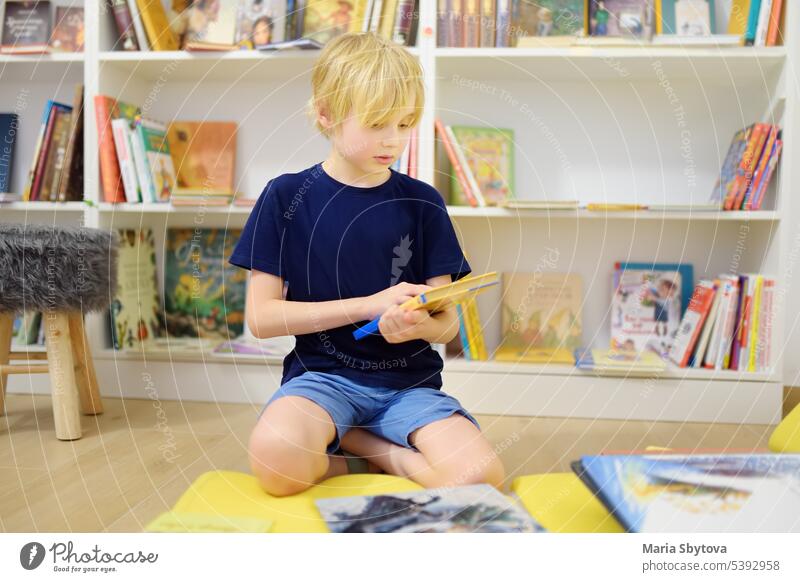 Ein Junge im Teenageralter blättert in einem Buch, während er in einer Schulbibliothek oder einer Buchhandlung am Bücherregal sitzt. Kluges Kind liest Abenteuerbuch