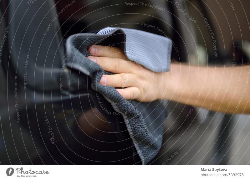 Ein reifer Mann reinigt sein Auto mit einem Lappen. Der Fahrer wäscht die Scheiben seines Autos mit einem Mikrofaser-Waschlappen. PKW Säuberung manuell männlich