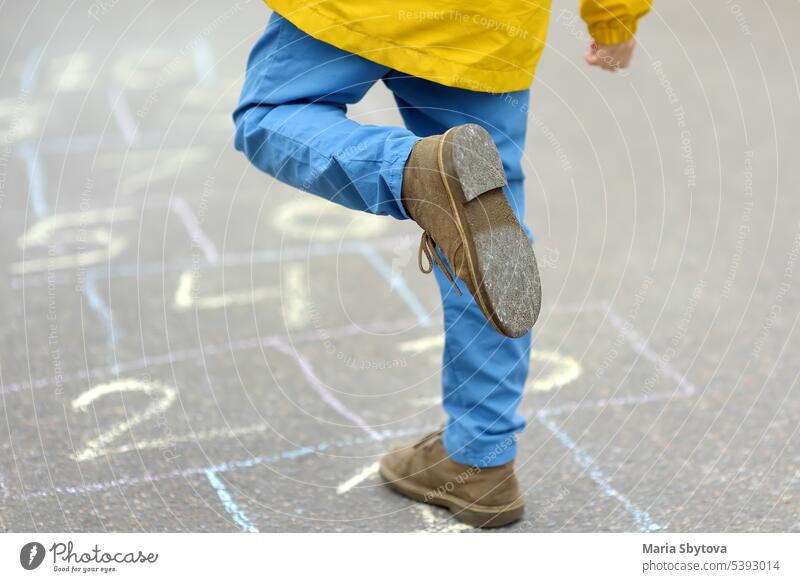 Kleiner Junge die Beine und hopscotch auf Asphalt gezeichnet. Kind spielt hopscotch Spiel auf dem Spielplatz am Frühlingstag. Himmel-und-Hölle-Spiel