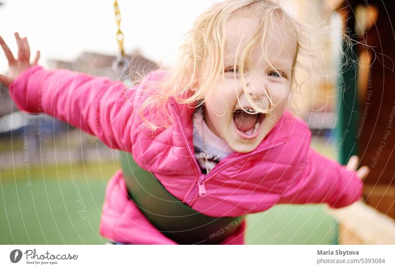 Nettes kleines Mädchen, das sich auf einem Spielplatz im Freien amüsiert. Frühling oder Sommer aktiven Sport Freizeit für Kinder. Kind auf Plastikschaukel