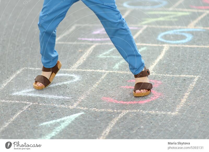 Kleiner Junge die Beine und hopscotch auf Asphalt gezeichnet. Kind spielt hopscotch Spiel auf dem Spielplatz am Frühlingstag. Himmel-und-Hölle-Spiel