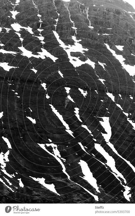 Schneereste auf einem Hügel auf Island Ostisland isländisch Seydisfjördur Felswand Felshügel steil Steilwand Schneeschmelze Felsformation Felsen nordisch