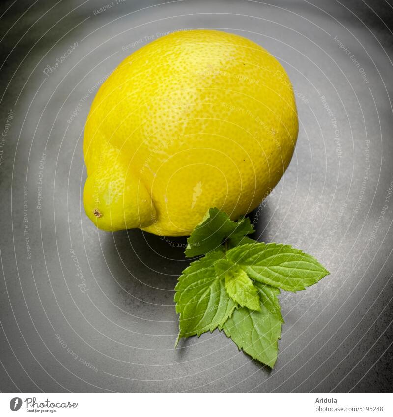 Eine Zitrone und Minzblätter auf einem schwarzen Teller Minze gelb grün ganze Zitrone Zitrusfrucht Limonade sauer Säure frisch Sommer Erfrischung