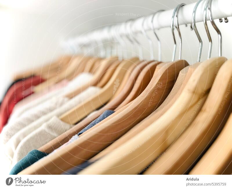 Kleiderbügel mit Kleidungsstücken hängen ordentlich nebeneinander auf einer Kleiderstange Oberteile Bügel Klamotten Bekleidung Mode Stoff Kleiderschrank