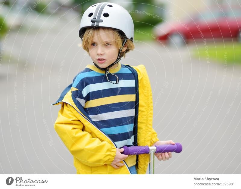 Kleiner Junge mit Schutzhelm fährt Roller. Das Kind langweilt sich ohne Freunde. Tretroller sicher Straße Verkehr Sicherheit Mitfahrgelegenheit Großstadt