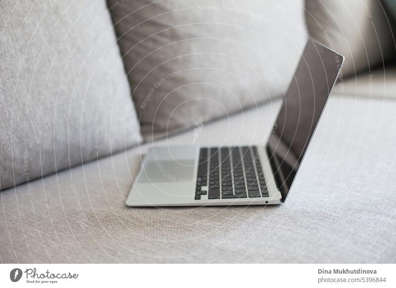 Silberner und schwarzer Laptop auf grauer Couch. Remote-Job-Arbeitsplatz, Arbeit von zu Hause aus. Hintergrund blanko Business Geschäftsmann lässig bequem