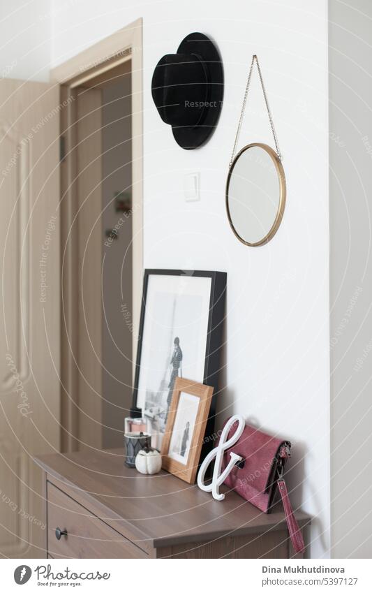 Elegantes Interieur Details eines Raumes mit weißen Wänden in der Wohnung. Wohnkultur mit schwarzem Hut, Fotografien, einer Handtasche und anderen Objekten.