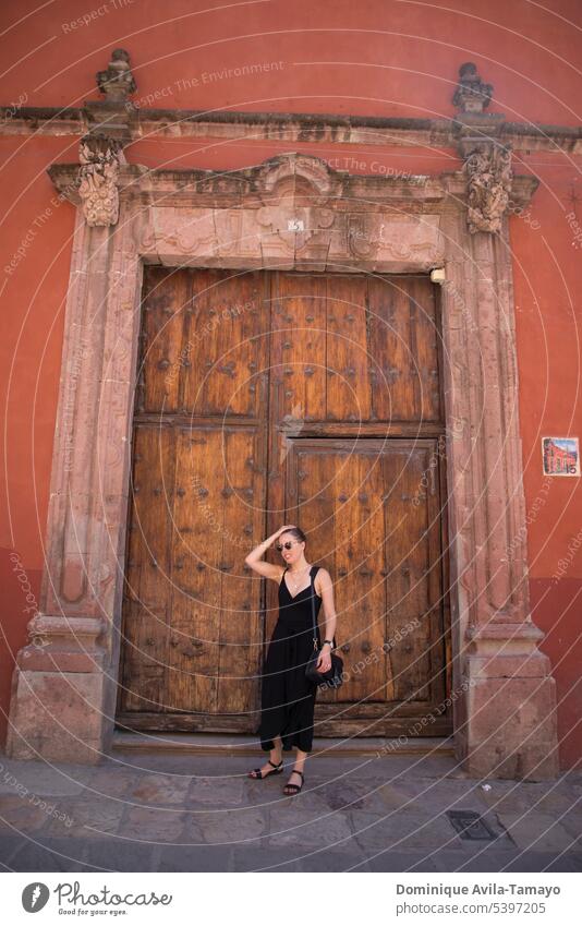 Frau im schwarzen Kleid vor einer Holztür yound schwarzes Kleid hölzern posierend alt Eingang Tür Außenaufnahme zugeklappt Eingangstür Junge Frau reisen