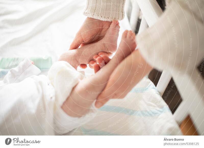 Eine frischgebackene Mutter hält sanft die kleinen Füße ihres Neugeborenen in der Wiege zu Hause Hände Baby neugeboren Beteiligung Beine neue Mutter verfrüht