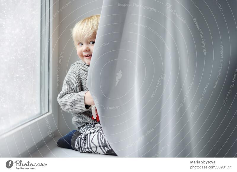 Kleiner Junge spielt zu Hause Baby Fenster Versteckspiel spielen Gardine Kind Spaß Spiel Schneefall Fensterbrett Kleinkind weiß süß Ausdruck Sitzen Fröhlichkeit