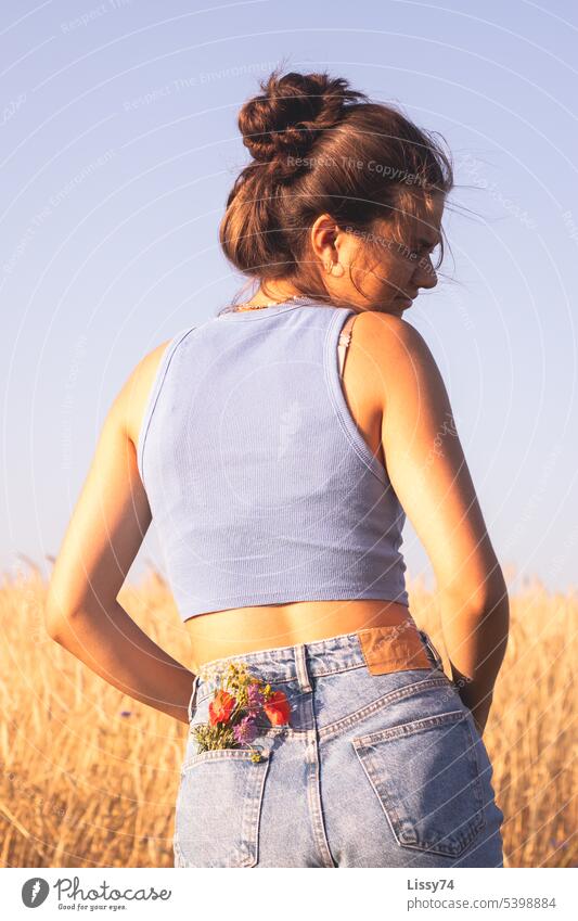 Am Feldrand stehendes Mädchen mit einem Blumenstrauß in der Hosentasche Natur Sommer Getreidefeld natürlich goldenes Licht jeans bunt Außenaufnahme farbig