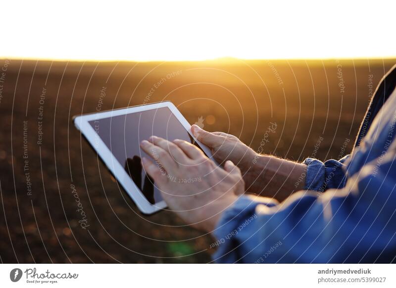 Ausschnitt aus den Händen eines männlichen Landwirts, der ein digitales Tablet auf einem gepflügten Feld zur Kontrolle der Bodenqualität und der Vorbereitung des Bodens für die Aussaat und den Anbau von Gemüse verwendet. Smart Farming Technologie und Landwirtschaft