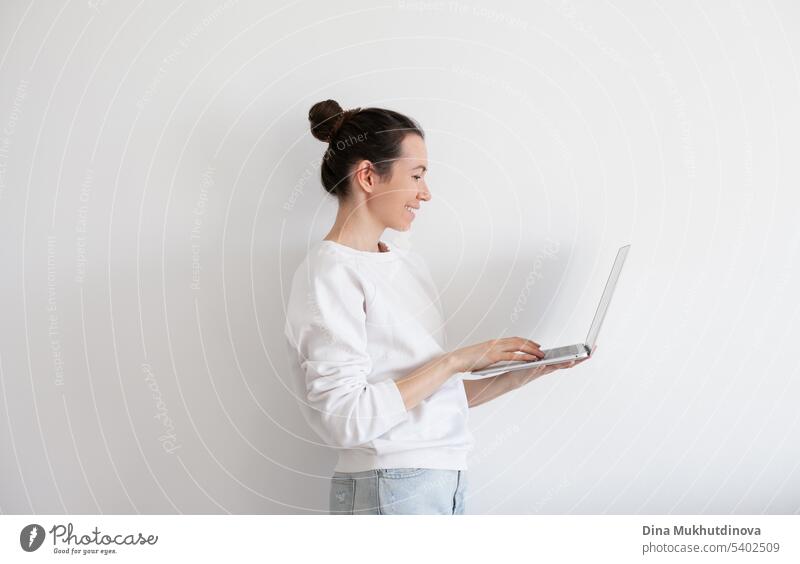 Junge Frau hält Laptop, arbeiten. Millennial Person in weißem Sweatshirt auf weißem Hintergrund. Menschen mit Technologie. schön Business Anruf Kaukasier heiter