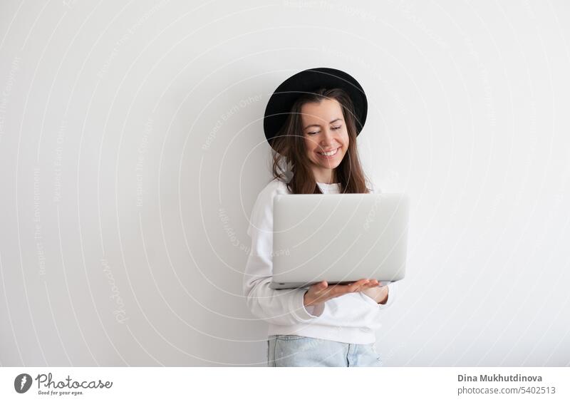 Junge Millennial-Frau mit schwarzem Hut und Laptop, die online arbeitet, weißer Hintergrund. Kopierraum links und rechts. schön Business Anruf Kaukasier heiter