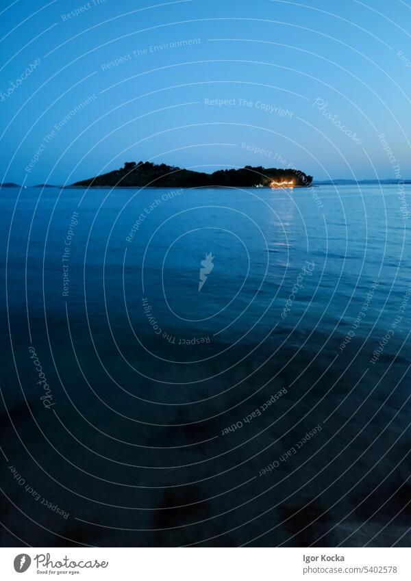 Kleine Insel im Meer am frühen Abend mit beleuchtetem Teil der Küste. MEER Nacht Lichter Ferien & Urlaub & Reisen Fernweh Sommerurlaub blau Wasser Himmel